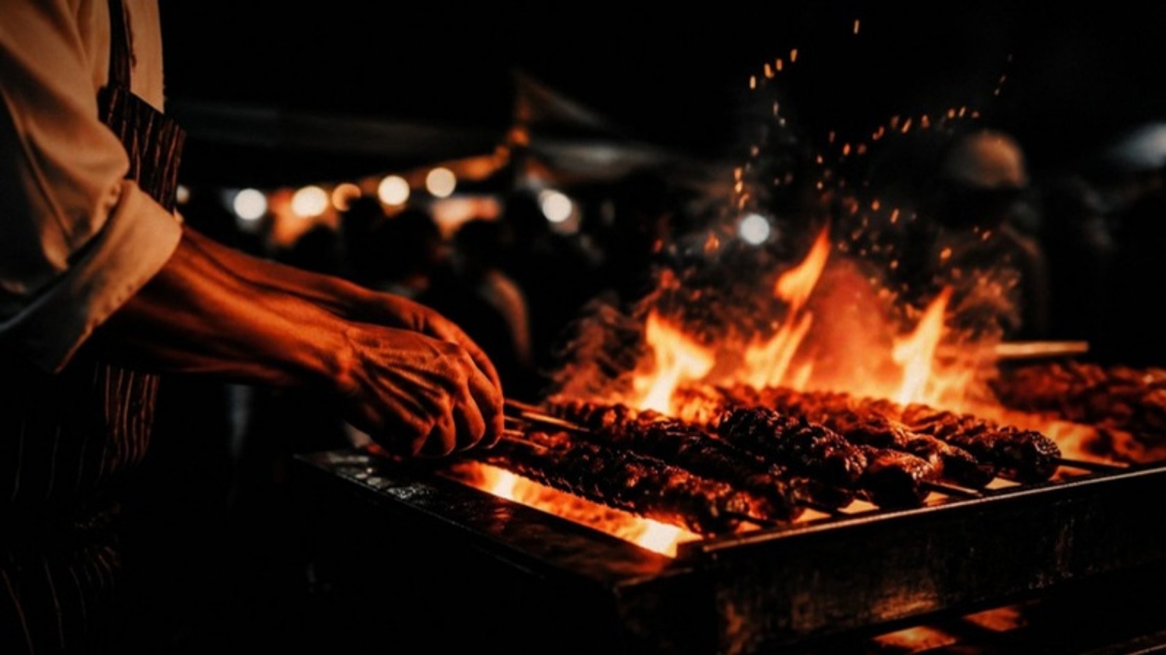 A cook turns skewers over open flame at a night festival