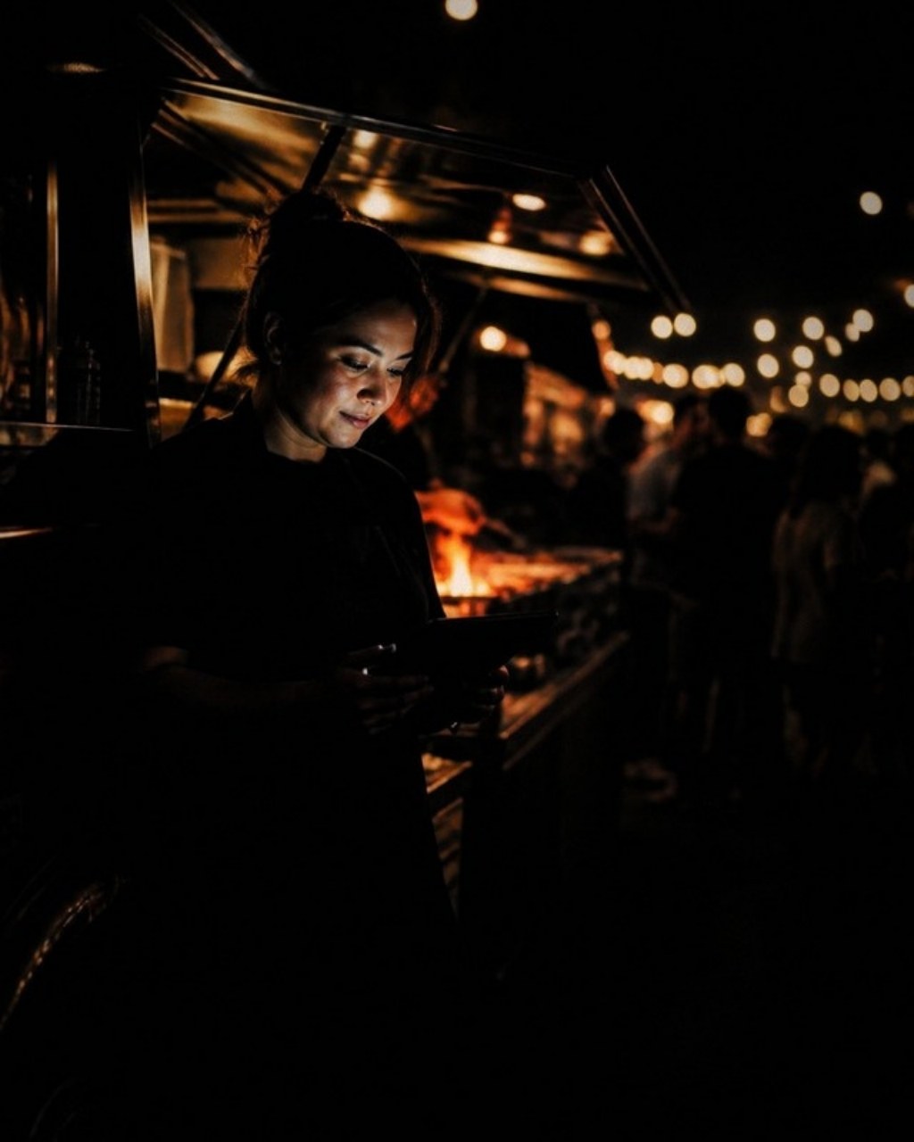 A food truck operator checks a tablet beside her truck at night