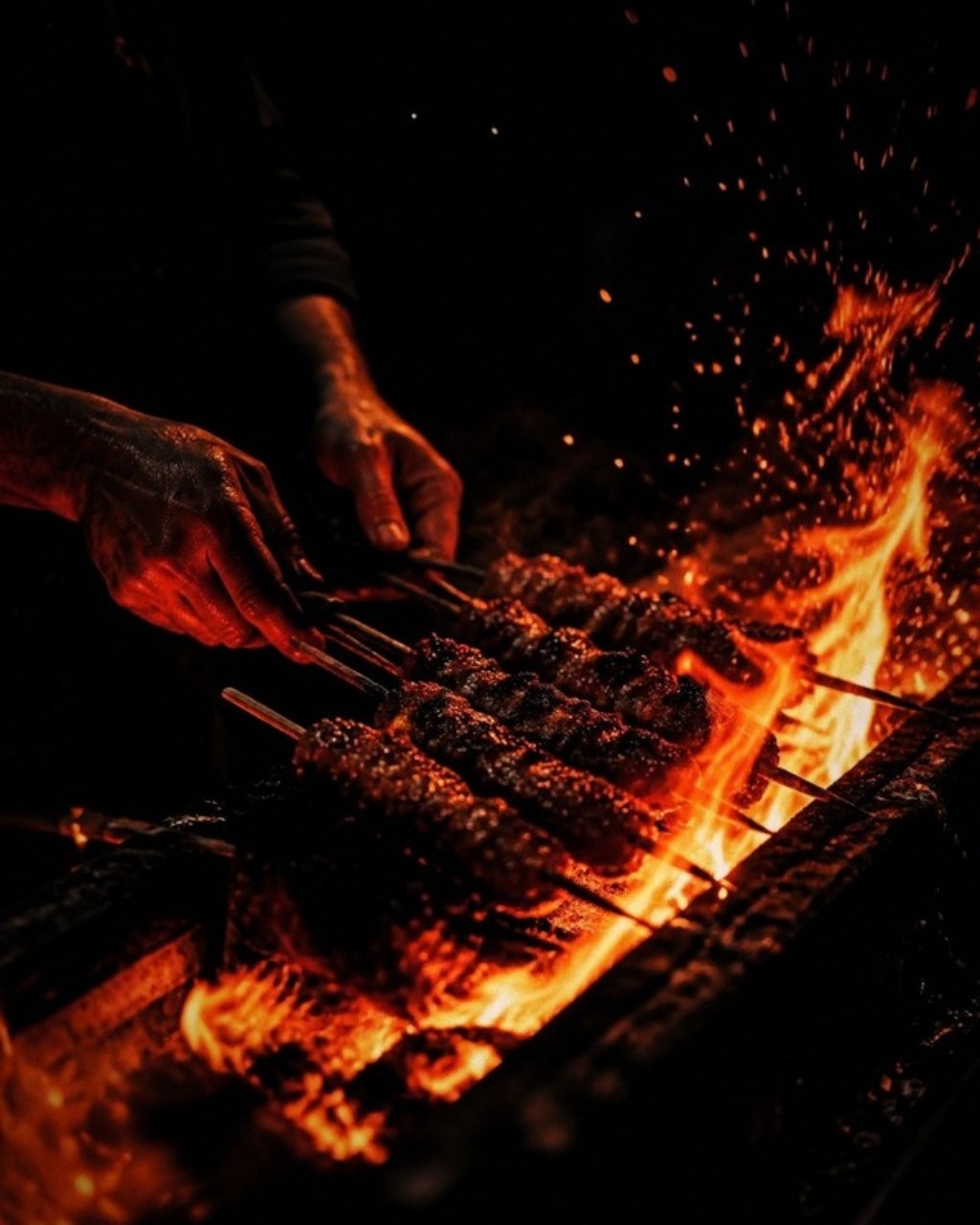 Hands working skewers over a flaming grill
