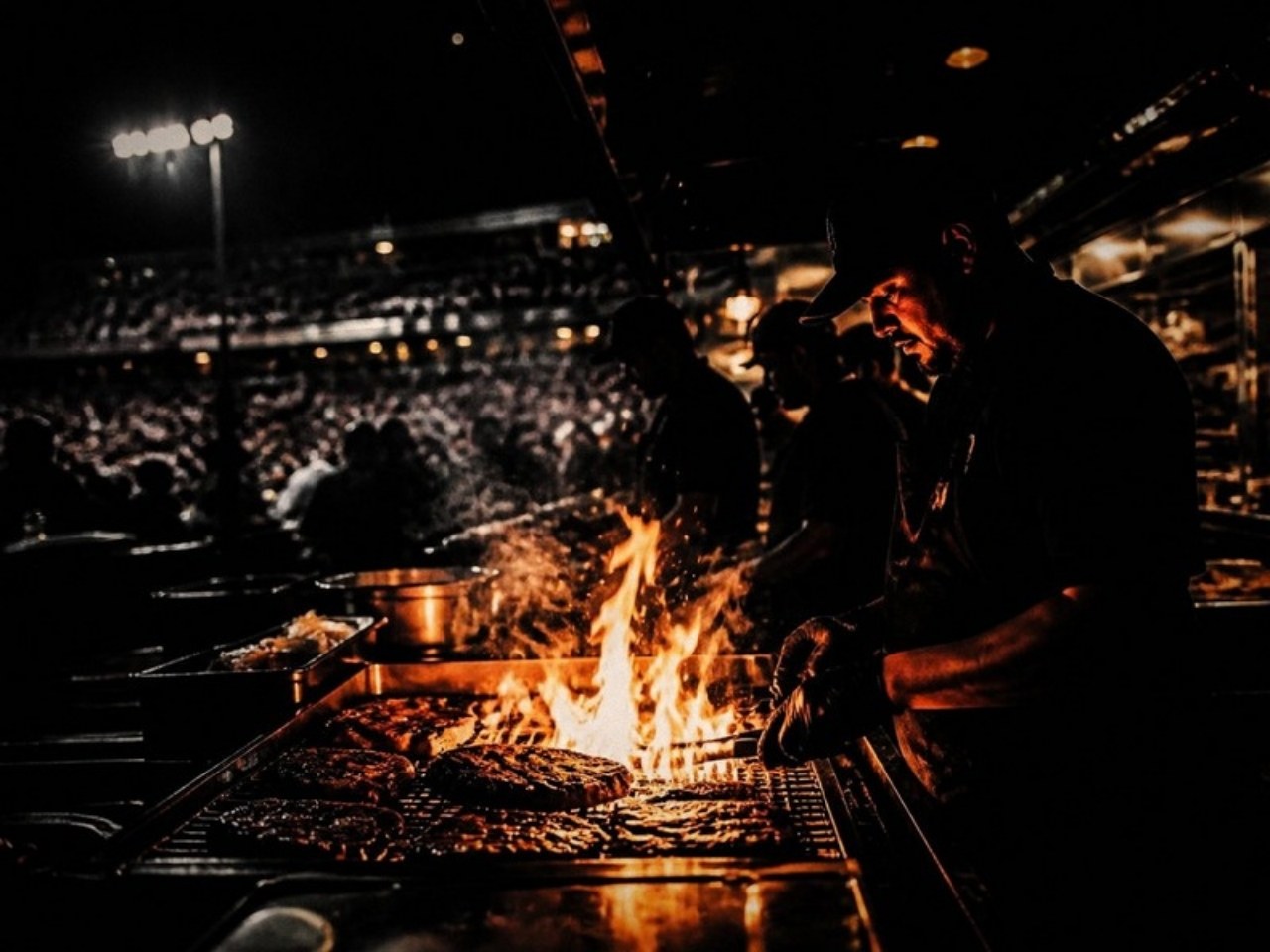 Cooks working a flaming grill at a stadium concession stand